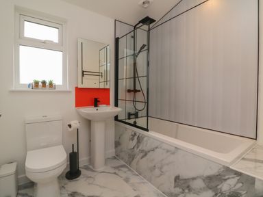 A bathroom with a toilet sink bathtub glass shower screen and a window with small plants at Cove Lodge in Ilfracombe
