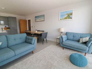 A living room with two blue sofas a wooden dining table with four grey chairs two paintings on the wall a lamp on a side table and a blue knitted pouf at 7 Warren Edge Close Bournemouth