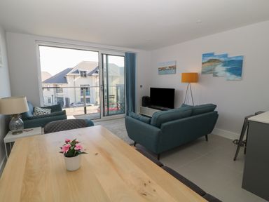 A living room with blue sofas a wooden table with a small plant a television and a sliding glass door at 7 Warren Edge Close in Bournemouth