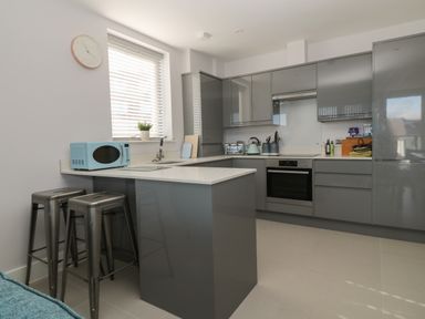 A modern kitchen with grey cabinets a blue microwave and a breakfast bar with two metal stools at 7 Warren Edge Close in Bournemouth
