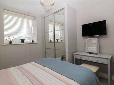 A bedroom with a bed a window with blinds a mirrored wardrobe a vanity table with a stool and a wall mounted television at 7 Warren Edge Close in Bournemouth