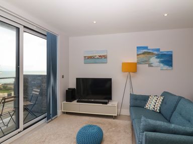 A living room with a blue sofa a television on a stand a yellow floor lamp and sliding glass doors leading to a balcony at 7 Warren Edge Close in Bournemouth