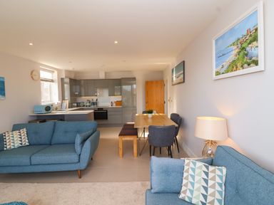 An open plan living room and kitchen with blue sofas and a wooden dining table at 7 Warren Edge Close Bournemouth
