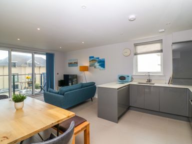 An open plan kitchen and living area with a wooden dining table blue sofa grey cabinets and a balcony at 7 Warren Edge Close in Bournemouth