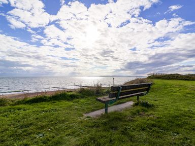 A bench on a grassy area overlooking the sea with a partly cloudy sky at 7 Warren Edge Close in Bournemouth