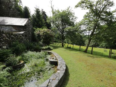 A garden with a stone pond and trees beside a stone building at Beaver Grove Cottage in Betws-Y-Coed