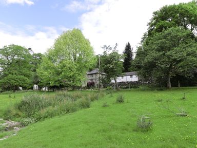 A grassy field with trees and a stone building in the background at Beaver Grove Cottage in Betws-Y-Coed