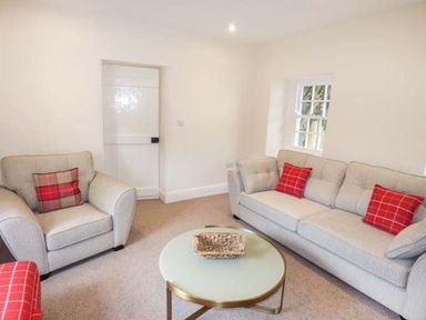 A living room with armchair and sofa with red checkered cushions and a round coffee table at Beaver Grove Cottage in Betws Y Coed