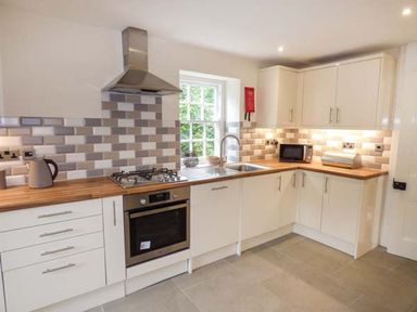 A kitchen with white cabinets wooden countertops a gas stove microwave and a sink at Beaver Grove Cottage in Betws-Y-Coed