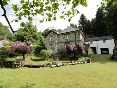 A stone cottage with garden furniture and trees at Beaver Grove Cottage in Betws-Y-Coed