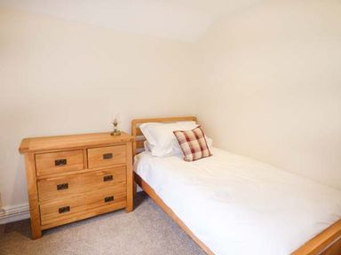 A bedroom with a single wooden bed and a wooden chest of drawers at Beaver Grove Cottage in Betws-Y-Coed