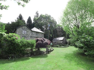 A stone house and a small stone building surrounded by grass trees and bushes at Beaver Grove Cottage in Betws-Y-Coed
