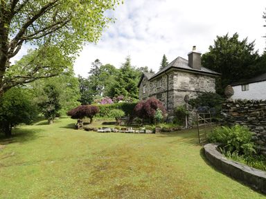 A stone house with a garden and trees surrounding it at Beaver Grove Cottage in Betws-Y-Coed