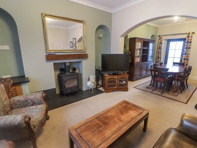 A living room with a wood stove television wooden coffee table dining table and chairs at Cheriton in Pembroke Dock