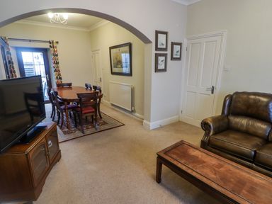 A living room with a brown leather sofa wooden coffee table and dining table with chairs at Cheriton in Pembroke Dock