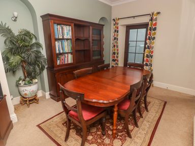 A dining room with a wooden dining table and chairs a bookshelf and a potted plant at Cheriton in Pembroke Dock