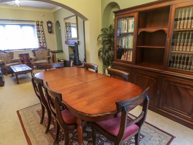 A dining room with a wooden table and chairs a large cabinet with books and two upholstered armchairs near a window at Cheriton in Pembroke Dock