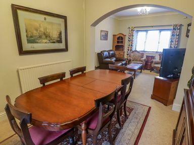 A dining area with a wooden table and chairs next to a living room with seating and a television at Cheriton in Pembroke Dock