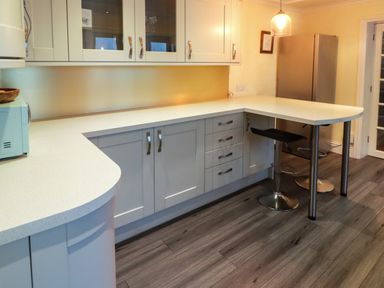 A kitchen with white countertops gray cabinets a microwave two stools a hanging light and a refrigerator at Cheriton in Pembroke Dock