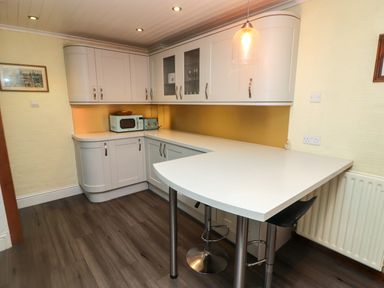 A kitchen with white cabinets a microwave a toaster a countertop bar with stools and a pendant light at Cheriton in Pembroke Dock