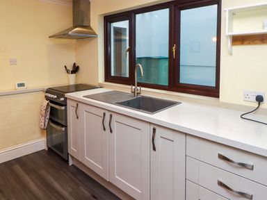 A kitchen with white cabinets a sink below two windows a stove with an oven and a range hood at Cheriton in Pembroke Dock
