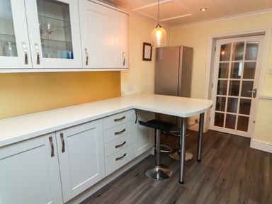 A kitchen with white cabinets a countertop a bar stool a hanging light and a glass door at Cheriton in Pembroke Dock