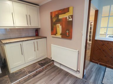 A kitchen area with white cabinets countertop and fire extinguisher next to a wall with an abstract painting and a radiator near a wooden door leading to another room at Cheriton Pembroke Dock