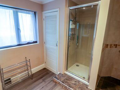 A bathroom with a glass shower enclosure a metal towel rack a window with sheer curtains and a closet door at Cheriton in Pembroke Dock