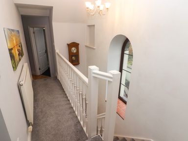 A carpeted hallway with a white railing and a wall clock near an arched window at Cheriton Pembroke Dock