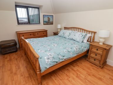 A bedroom with a wooden bed with floral bedding two wooden bedside tables with lamps a wooden dresser a window and a painting on the wall at Cheriton in Pembroke Dock