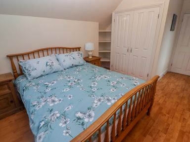 A bedroom with a wooden bed frame a blue floral bedspread wooden nightstands with a lamp and a white closet with shelves at Cheriton in Pembroke Dock