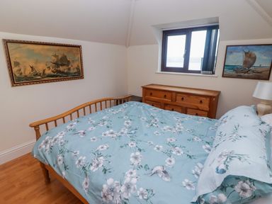 A bedroom with a wooden bed with floral bedding a wooden dresser below a window and two paintings on the walls at Cheriton in Pembroke Dock