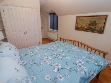 A bedroom with a wooden bed with floral bedding a white double-door wardrobe a lamp a radiator and a painting of ships on the wall at Cheriton in Pembroke Dock