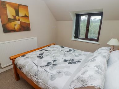 A bedroom with a wooden bed with leaf patterned bedding a window with a view of trees a radiator a bedside lamp and abstract wall art at Cheriton in Pembroke Dock
