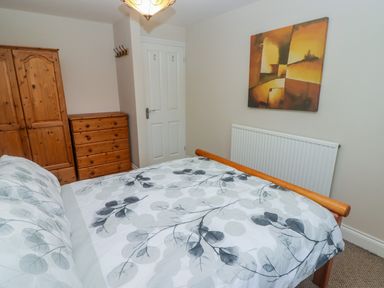 A bedroom with a bedfroom set including a wardrobe and chest of drawers and a bed with patterned bedding at Cheriton in Pembroke Dock