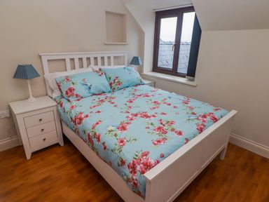 A bedroom with a white bed frame and floral bedding beside two white nightstands with blue lamps at Cheriton in Pembroke Dock