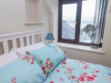 A bedroom with a white bed frame blue floral bedding a blue lamp and a window showing outside view at Cheriton in Pembroke Dock