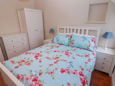 A bedroom with a bed floral bedspread white furniture and two blue lamps at Cheriton in Pembroke Dock
