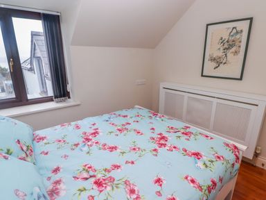 A bedroom with a bed covered in floral bedding next to a window and a framed picture on the wall at Cheriton in Pembroke Dock