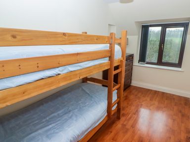 A bedroom with wooden bunk beds a chest of drawers and a window overlooking trees at Cheriton in Pembroke Dock