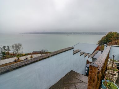 Stone steps with white walls and wooden railing leading down to a waterfront with trees and planters at Cheriton in Pembroke Dock