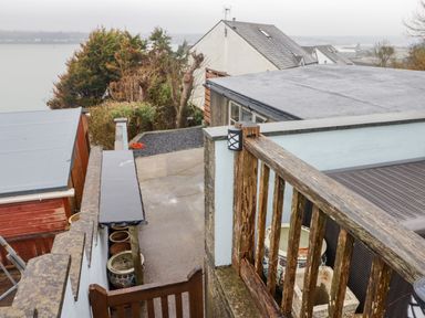 An outdoor area with a wooden railing, potted plants, a concrete path, and houses in the background at Cheriton in Pembroke Dock