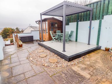An outdoor patio with a pergola table and chairs a wooden shed and stone pathways at Cheriton in Pembroke Dock