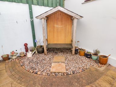 A small garden area with a wooden shelter surrounded by potted plants and a stone path at Cheriton in Pembroke Dock