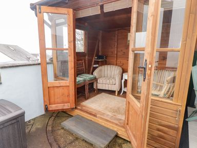 A wooden garden room with striped armchairs a wooden chair with cushions a small white side table and a rug at Cheriton in Pembroke Dock
