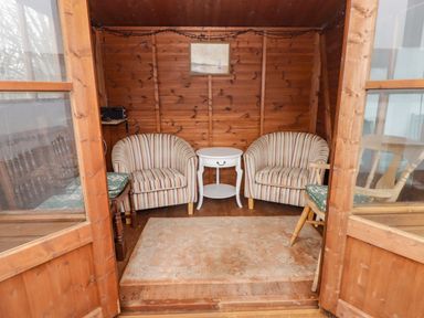 A wooden room with two striped armchairs a small white table a wooden chair with a cushion and a rug on the wooden floor at Cheriton in Pembroke Dock