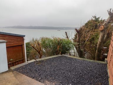A gravel yard with trimmed bushes and trees overlooking a body of water with a boat and distant hills at Cheriton in Pembroke Dock