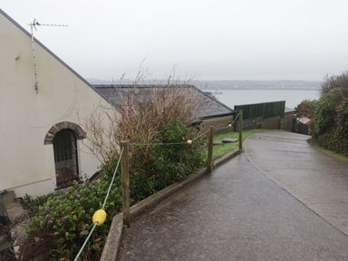 A sloping paved driveway with a rope fence and bushes beside a house overlooking water at Cheriton in Pembroke Dock