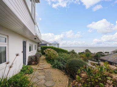 A pathway with hexagonal stones and plants beside a white house with a view of the sea and neighboring houses at Waves Edge in Looe