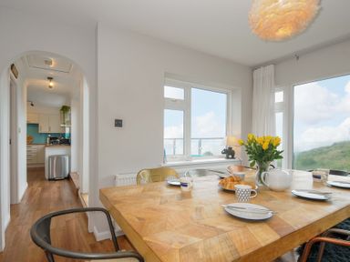A dining room with a wooden table set with cups, plates, a teapot, croissants, and yellow flowers in a vase at Waves Edge in Looe